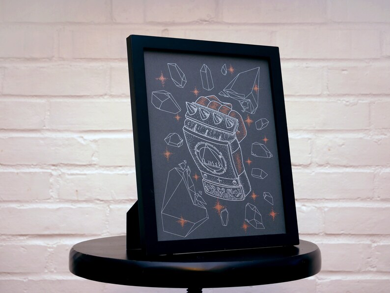 May include: A black framed print with a white illustration of a hand wearing a spiked gauntlet. The gauntlet is surrounded by white geometric shapes on a dark gray background.