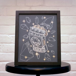 May include: A black framed print with a white illustration of a hand wearing a spiky gauntlet. The gauntlet is surrounded by white geometric shapes that resemble crystals. The background is a dark gray.