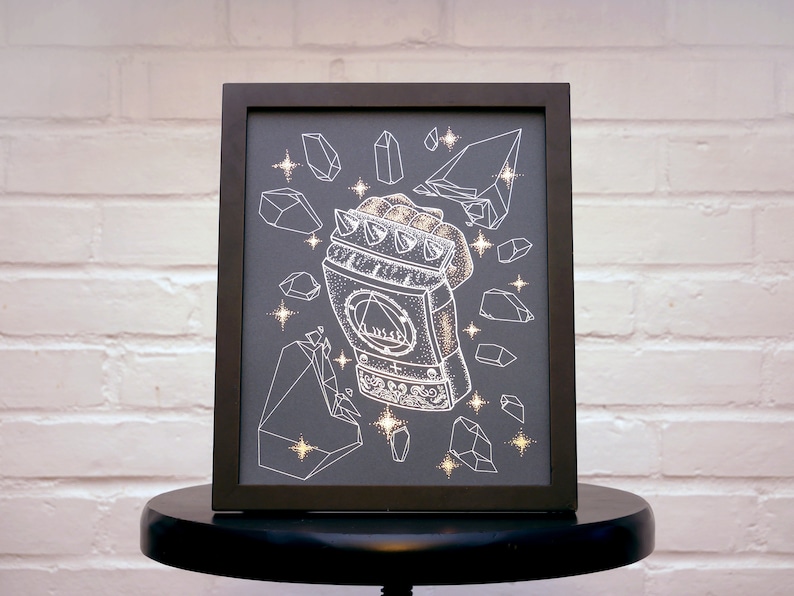 May include: A black framed print with a white illustration of a hand wearing a spiky gauntlet. The gauntlet is surrounded by white geometric shapes that resemble crystals. The background is a dark gray.