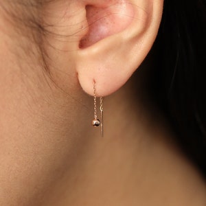 Puede incluir: Un par de pendientes de cadena de oro con una pequeña bola al final de cada cadena.