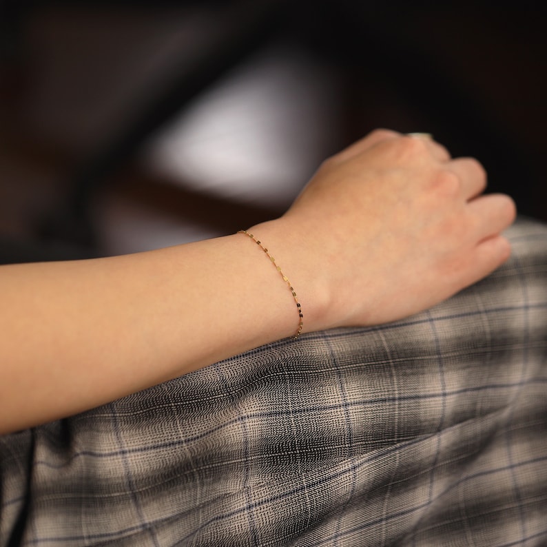 Puede incluir: Un delicado brazalete de cadena de oro con un patr&oacute;n de eslabones cuadrados.