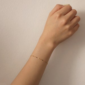 Puede incluir: Un delicado brazalete de cadena dorada con peque&ntilde;as cuentas negras.