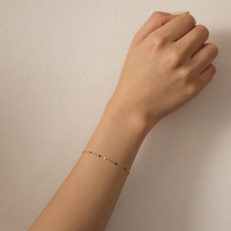 Puede incluir: Un delicado brazalete de cadena dorada con peque&ntilde;as cuentas negras.