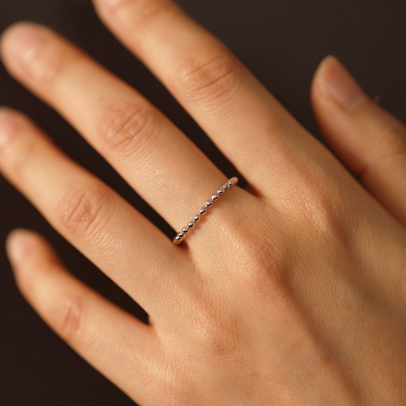 K&ouml;nnte beinhalten: Ein zarter Silberring mit Perlenmuster. Der Ring wird an einem Finger getragen.