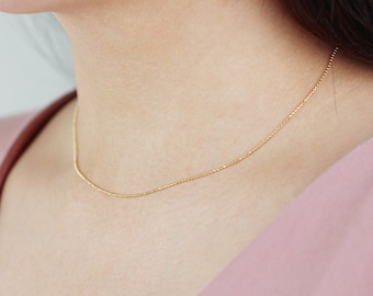 May include: A delicate gold chain necklace, worn by a model, with a simple design.