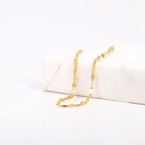 Puede incluir: Un collar de cadena de oro con un delicado dise&ntilde;o de eslabones ovalados. La cadena se muestra sobre una superficie blanca.