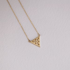 May include: A gold necklace with a delicate triangle pendant featuring a geometric pattern of circles.