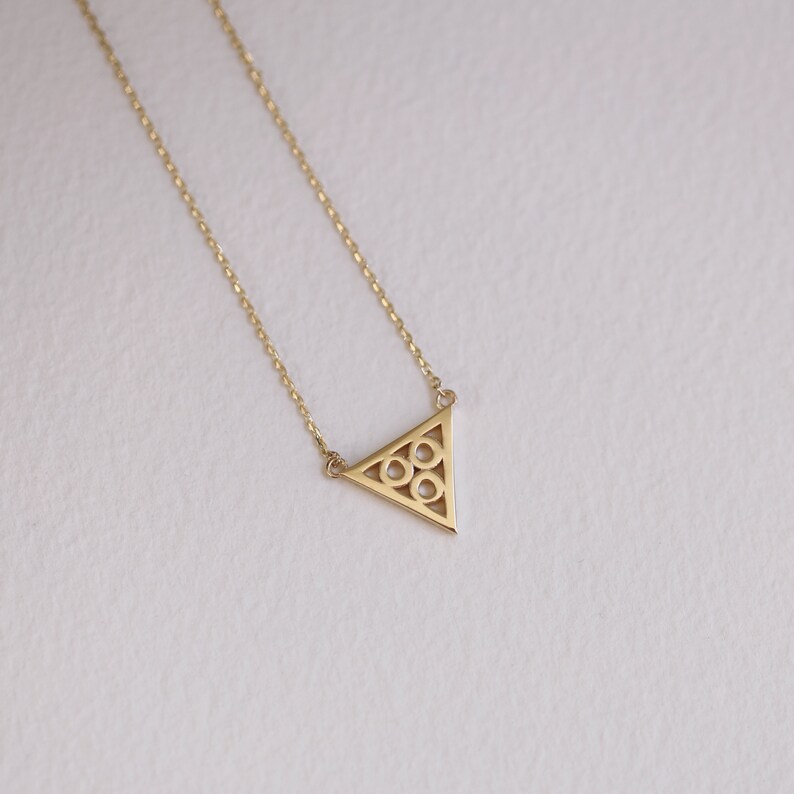 May include: A gold necklace with a delicate triangle pendant featuring a geometric pattern of circles.