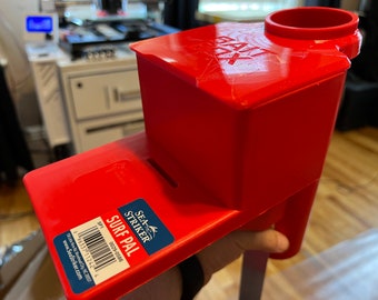 May include: Red plastic surf fishing rod holder with a label that reads "Sea Striker Surf Pal".