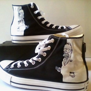 Puede incluir: Par de zapatillas altas de lona, ​​blancas y negras, con un diseño de personaje de dibujos animados. Las zapatillas tienen cordones blancos, puntera de goma blanca y suela blanca con una franja negra.