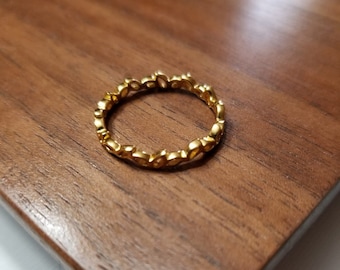 May include: A gold ring with a delicate design of small, rounded shapes. The ring is made of metal and has a smooth, polished finish.