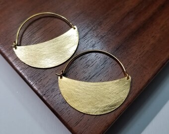 May include: A pair of gold hoop earrings with a half-moon shape. The earrings have a brushed finish.