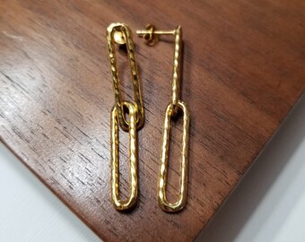 May include: A pair of gold-toned dangle earrings with a chain link design. The earrings are made of two connected oval-shaped links.