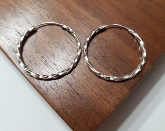 May include: A pair of silver hoop earrings with a twisted design. The earrings are on a wooden surface.