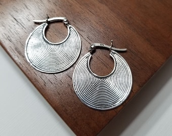 May include: A pair of silver hoop earrings with a textured, circular design. The earrings have a slightly hammered finish and are made of metal.
