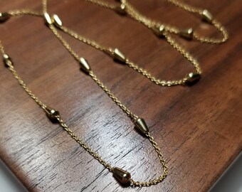 May include: A gold chain necklace with teardrop-shaped beads. The necklace is on a wooden surface.