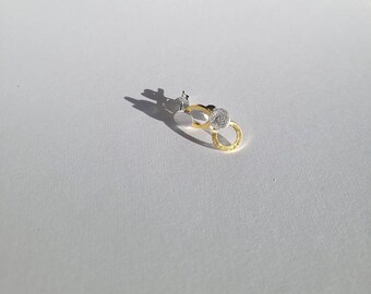 May include: A pair of silver and gold earrings with a circle design. The earrings are small and delicate.