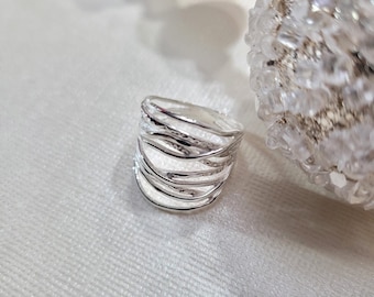 May include: A silver ring with a unique, multi-layered design. The ring is made of multiple thin bands that are intertwined and textured.