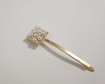 May include: A gold hair clip with a square-shaped pearl embellishment. The clip is made of metal and has a simple design.