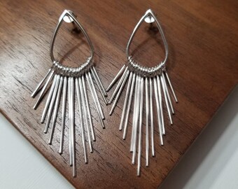May include: A pair of silver dangle earrings with a teardrop-shaped top and multiple thin, silver rods extending from the bottom.