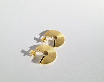May include: A pair of gold-toned earrings with a semi-circle shape and a black line across the center.