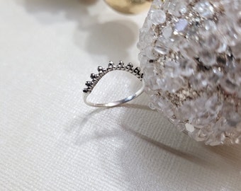 May include: A silver ring with a beaded design. The ring is curved into an arch shape.