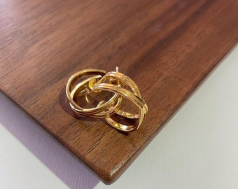 May include: A pair of gold hoop earrings with a double-layered design. The earrings are made of a thick, sturdy metal and have a polished finish.