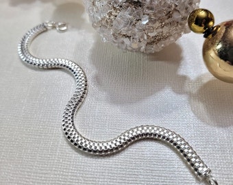 May include: A silver chain bracelet with a textured, snake-like design. The bracelet is made of small, interlocking links that create a smooth, flowing look.
