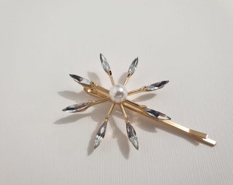 May include: Gold hair clip with a pearl in the center and clear rhinestones radiating out from the pearl.