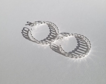 May include: A pair of silver hoop earrings with a chain link design. The earrings are laying on a white surface.