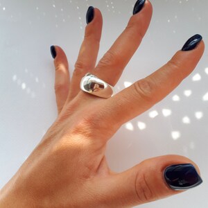 May include: A polished silver-tone ring with a wide, smooth, and domed band. The metal surface is highly reflective, showing a clear mirror-like finish that catches the light. The ring features a solid, continuous construction with no visible stones.