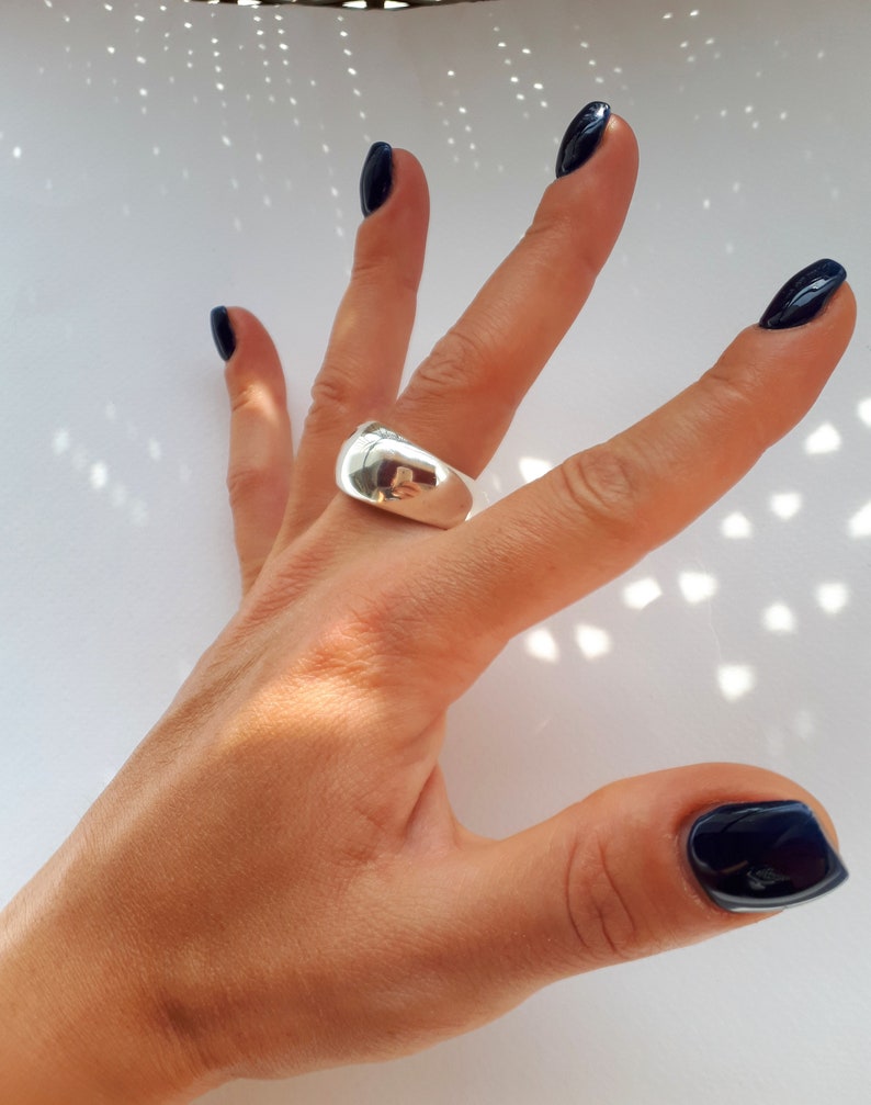 May include: A polished silver-tone ring with a wide, smooth, and domed band. The metal surface is highly reflective, showing a clear mirror-like finish that catches the light. The ring features a solid, continuous construction with no visible stones.