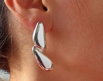 May include: A pair of silver statement earrings with a unique, abstract design. The earrings are made of two curved, smooth, silver pieces that are connected together.