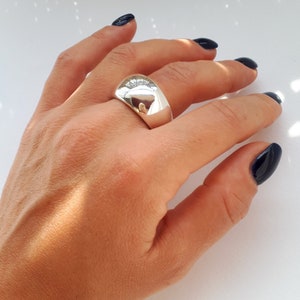 May include: A wide, polished silver-tone dome ring with a smooth, reflective surface. The band features a thick, rounded profile that tapers slightly toward the palm, creating a bold, solid appearance on the finger with high-shine metallic finish.