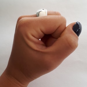 May include: A polished silver signet ring with a smooth, rounded rectangular face. The ring features a reflective metallic surface and is worn on the index finger, showcasing a clean, minimalist design with no engravings or additional embellishments.