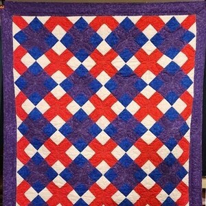 Puede incluir: Una colcha con un patrón geométrico de cuadrados rojos, blancos y azules. La colcha está hecha con una variedad de telas y tiene una textura acolchada.