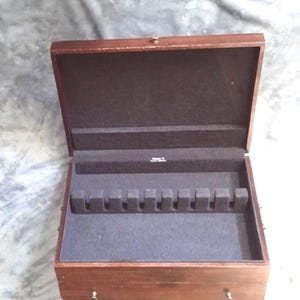 May include: Open wooden silverware storage box with a dark brown exterior and a dark gray felt interior. The box has a hinged lid and a series of slots for holding utensils. The box is empty.