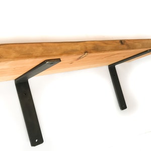 K&ouml;nnte beinhalten: Ein Holzregal mit nat&uuml;rlicher Holzoptik und zwei schwarzen Metallkonsolen. Das Regal besteht aus einem einzigen St&uuml;ck Holz mit einer lebenden Kante.