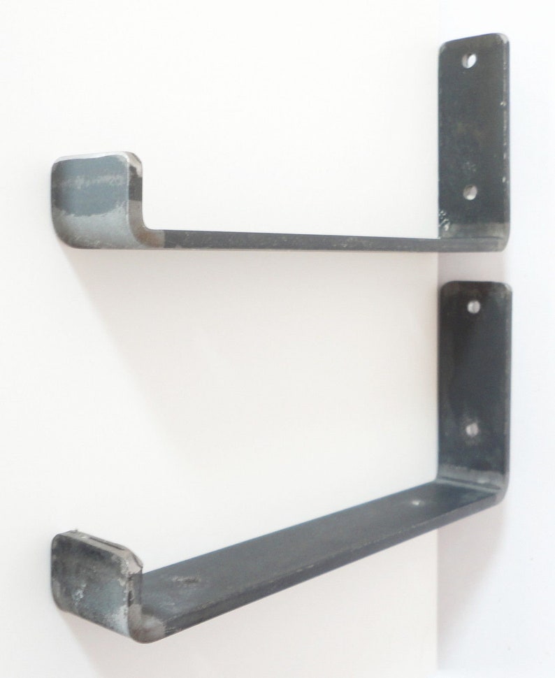 May include: Two black metal shelf brackets with a curved front edge. The brackets are mounted to a white wall.