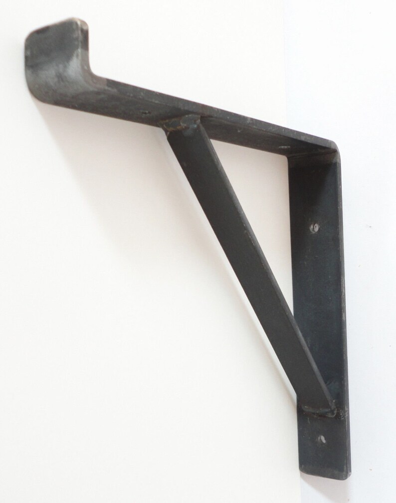 May include: A black metal shelf bracket with a triangular support. The bracket is mounted to a white wall.