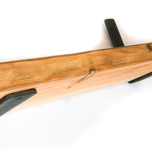 K&ouml;nnte beinhalten: Ein Holzregal mit einer nat&uuml;rlichen Holzoptik und schwarzen Metallkonsolen. Das Regal ist an einer Wand montiert.