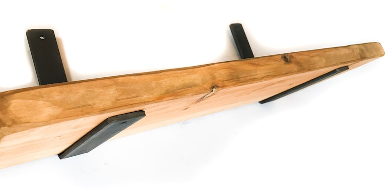 K&ouml;nnte beinhalten: Ein Holzregal mit einer nat&uuml;rlichen Holzoptik und schwarzen Metallkonsolen. Das Regal ist an einer Wand montiert.