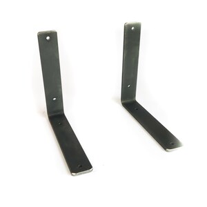 K&ouml;nnte beinhalten: Zwei schwarze Metall-Regalhalterungen mit jeweils vier L&ouml;chern. Die Halterungen sind L-f&ouml;rmig und haben eine matte Oberfl&auml;che.
