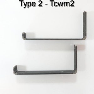 May include: Two black metal shelf brackets, each with a 90-degree angle and a flat surface for shelf support. The brackets are mounted on a white wall. The text "Type 2 - Tcwm2" is visible at the top of the image.