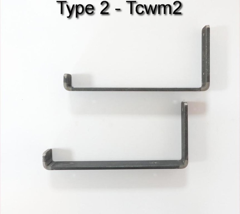 May include: Two black metal shelf brackets, each with a 90-degree angle and a flat surface for shelf support. The brackets are mounted on a white wall. The text "Type 2 - Tcwm2" is visible at the top of the image.