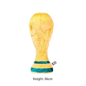 May include: A plush toy shaped like the FIFA World Cup trophy, featuring a golden yellow upper section with embossed globe details and a teal base with swirling patterns. The base includes the text FIFA WORLD CUP. It measures 36 cm in height.