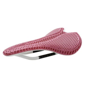 May include: A pink bicycle saddle with a perforated design. The saddle has a white and black support structure with measurement markings. The saddle is designed for comfort and performance.