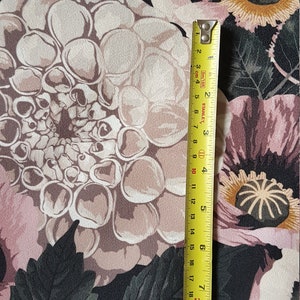 May include: Black fabric with a floral print featuring large pink, white, and brown flowers. A yellow measuring tape is placed vertically on the right side of the image.