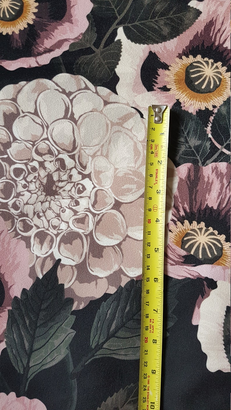 May include: Black fabric with a floral print featuring large pink, white, and brown flowers. A yellow measuring tape is placed vertically on the right side of the image.