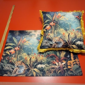 May include: A cushion and a rectangular mat with a jungle design, including a leopard, flowers, and butterflies. The cushion has a yellow fringe. The colour scheme features greens, oranges, and blues.